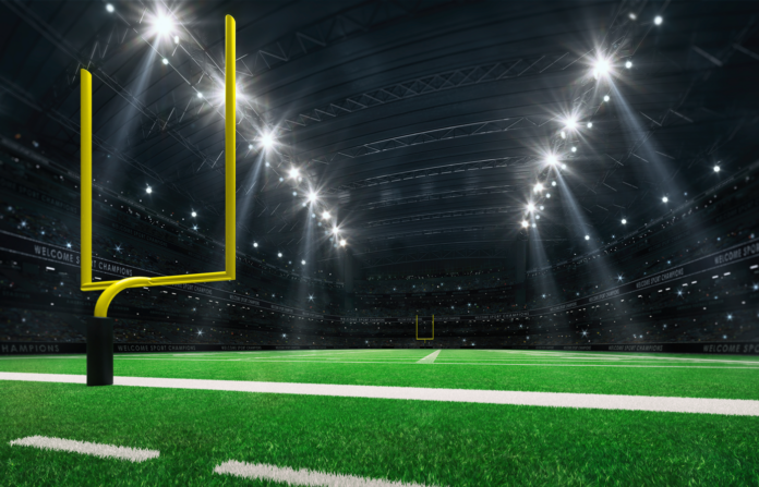 American football stadium with yellow goal posts, grass field and fans at playground view.